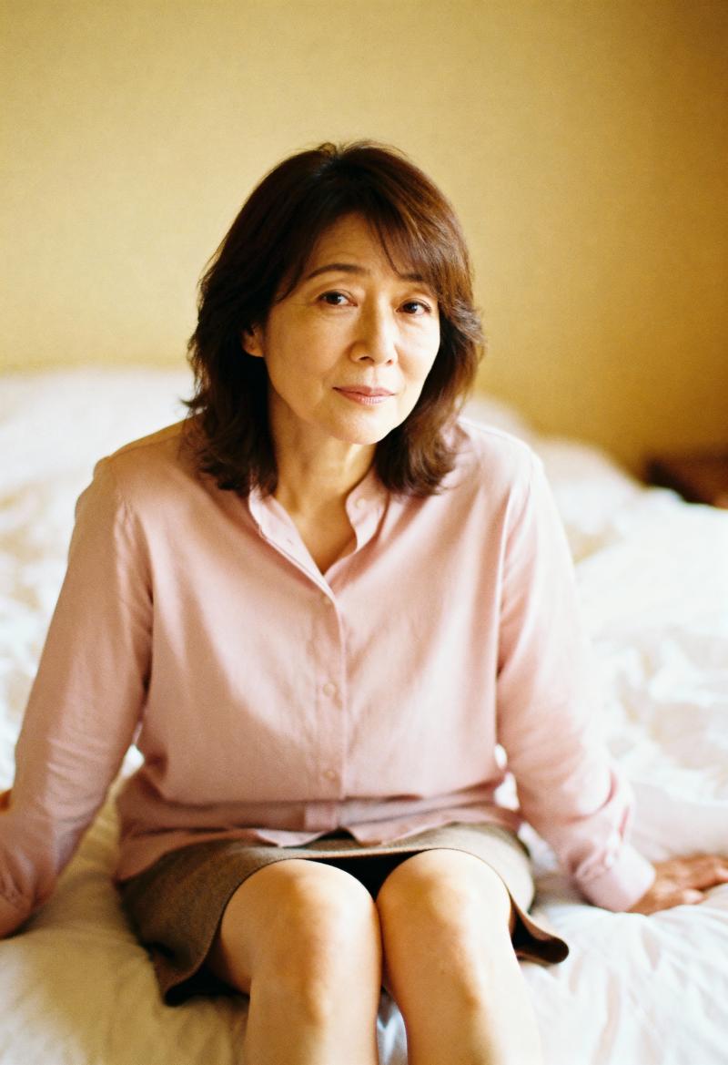柔らかく暖かい光の中でベッドに座る中年のアジア人女性のポートレート。