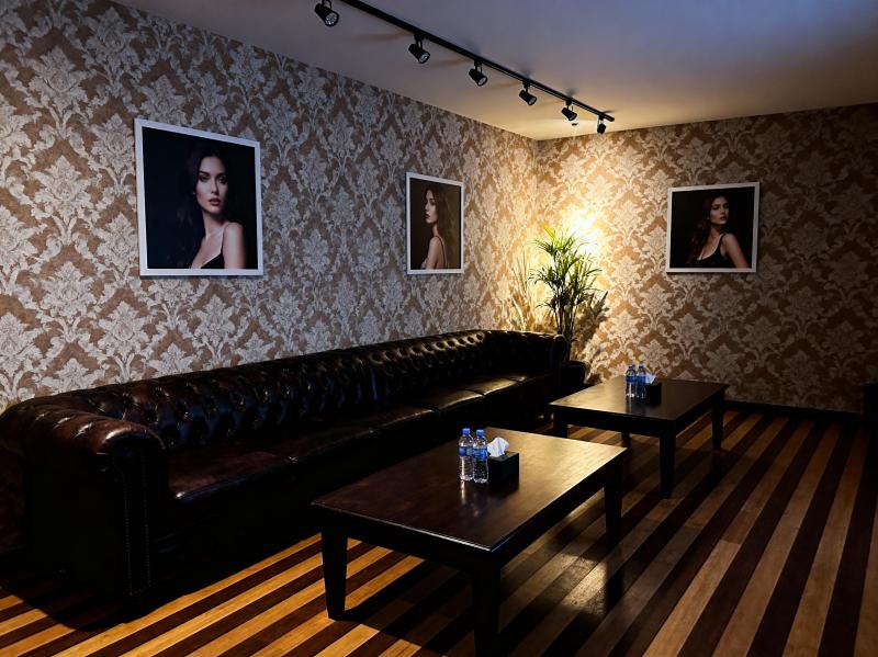 薄暗い部屋に、茶色の革張りのソファ、水の入ったボトルが置かれた 2 つの木製テーブル...。