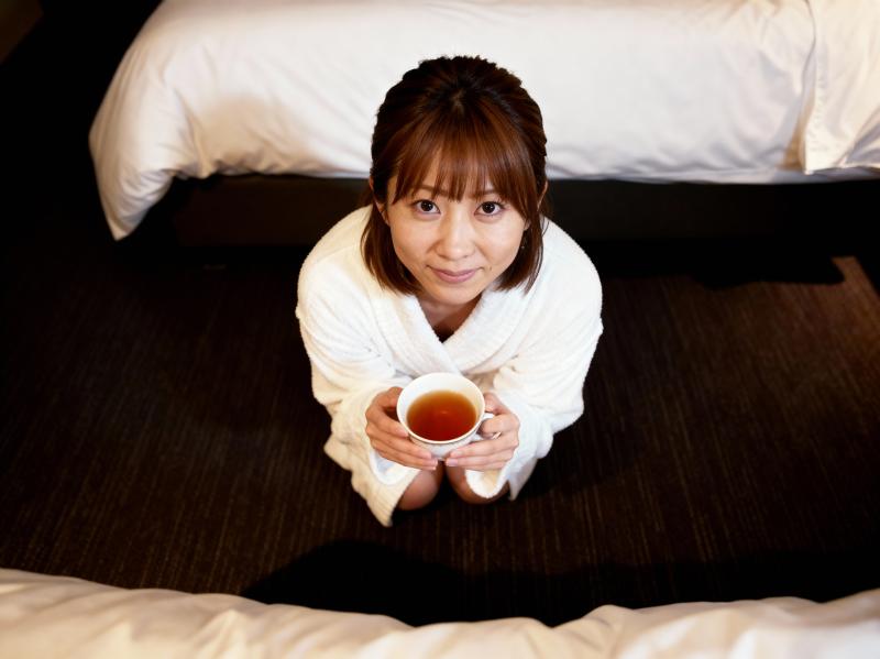 白いローブを着た女性が暗いカーペット敷きの床にひざまずいて、手にお茶を持っています。