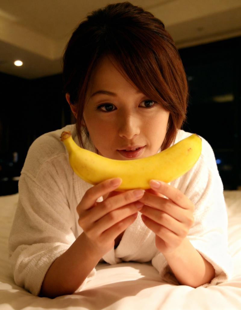 ベッドに横たわり、顔の前にバナナを持った若い女性。