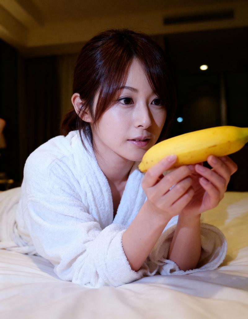 白いバスローブを着た若い女性がベッドに横たわり、黄色のカボチャを持ち、中立的な表情で...。