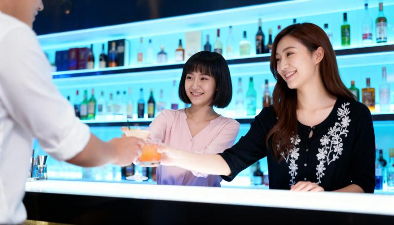 カラフルなアルコールのボトルを背景に、薄暗いバーのバーカウンターで握手する 2 人の...。