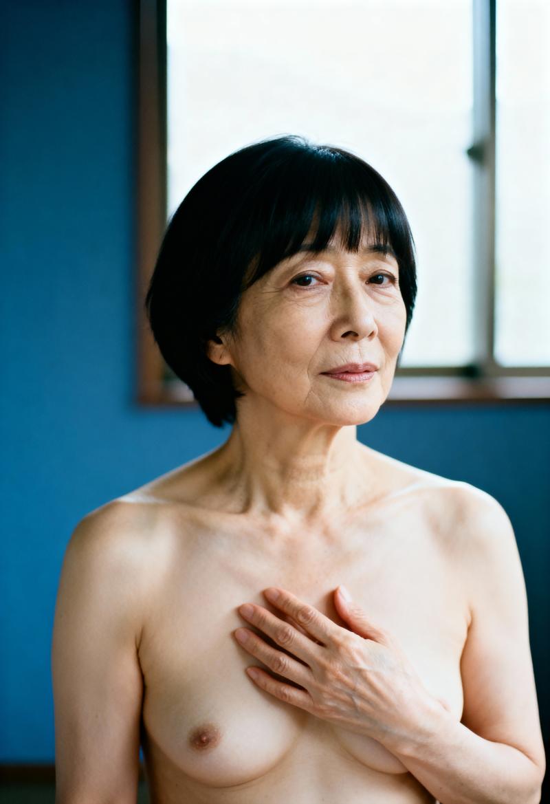背景に窓のある青い壁の前に立つ、短い黒のボブヘアをした年配のアジア人女性のポートレート。