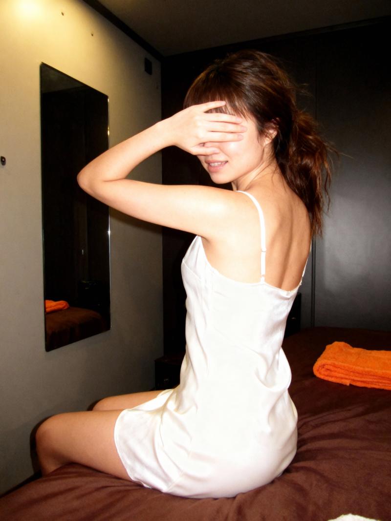 白いスリップドレスを着てベッドに座り、目を手で覆っている若い女性を横から撮った写実的な写真。