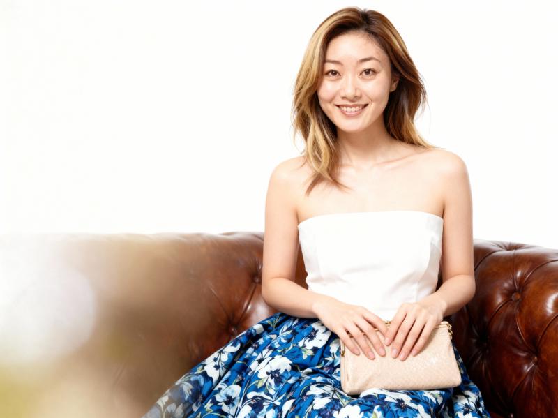 白いストラップレスのトップスと青い花柄のスカートを着て、リラックスしたポーズで茶色の...。