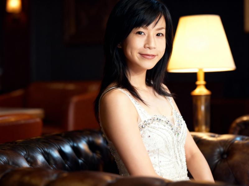 薄暗い部屋で茶色の革張りのソファに座り、白いビーズのドレスを着た女性のポートレート。