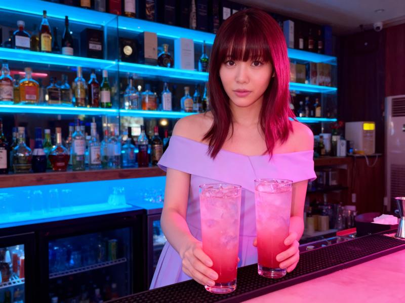 バーの後ろに立ち、ピンクのドリンクを 2 杯持っている若い女性を正面カメラのアングル...。