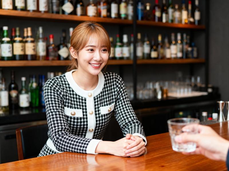 白い襟と金ボタンが付いた黒と白の千鳥格子のジャケットを着て、バーカウンターにグラスを...。