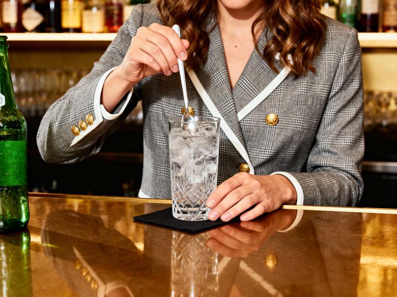 バーに座り、氷とスプーンを入れた水の入ったグラスを持っている、グレーのチェック柄のブ...。