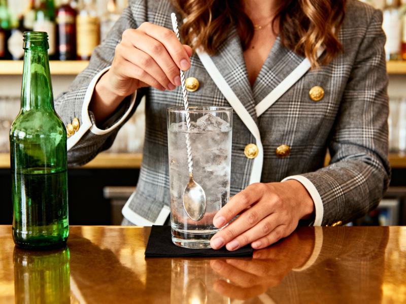 バーカウンターのグラスに水を注ぐバーテンダーの手に焦点を当てた、ローアングルからのク...。