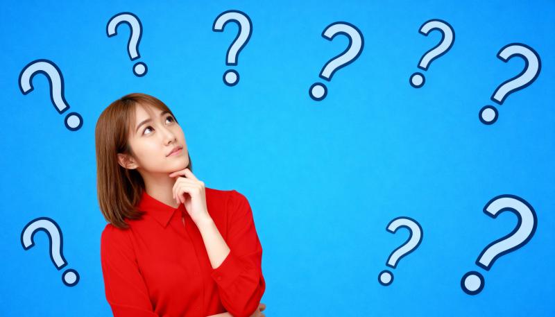 赤いシャツを着た長い茶色の髪の若い女性が、あごを手に当てて画像の中央に立って、思慮深...。