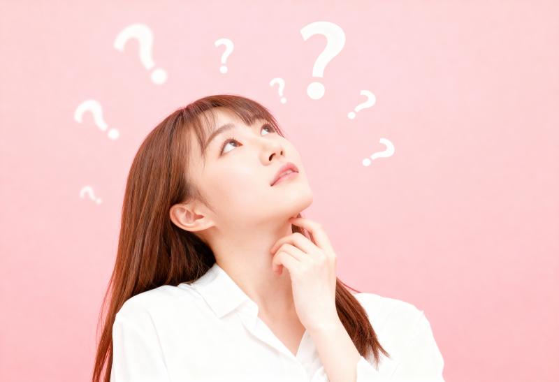 柔らかいピンクの背景に、白いブラウスを着た長い茶色の髪の若い女性が、頭上に疑問符を浮...。