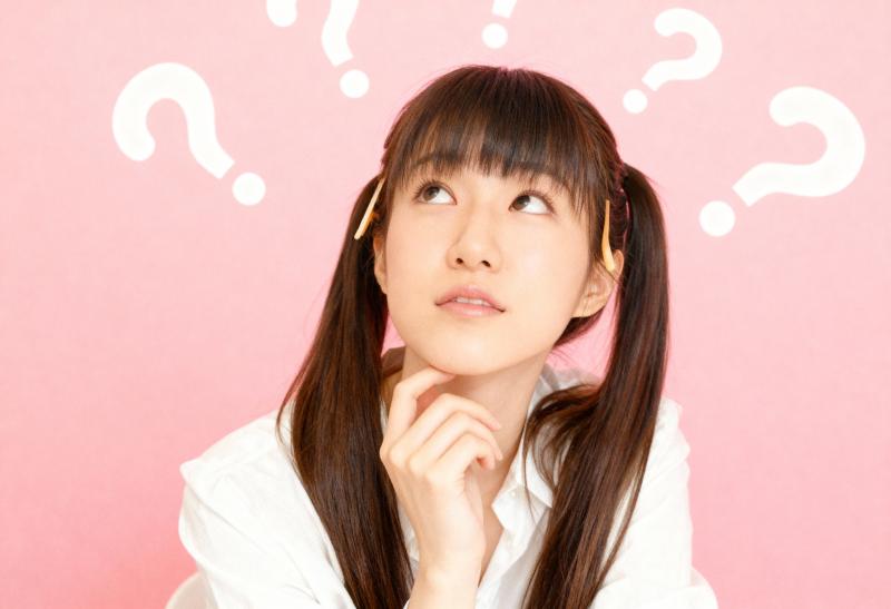 ピンクの背景に疑問符で囲まれた、長い茶色の髪と思慮深い表情をした若いアジア人女性を横...。