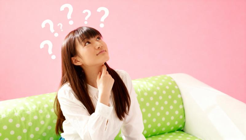 頭上に疑問符が付いたピンクの壁の前で緑の水玉模様のソファに座り、思慮深い表情で見上げ...。