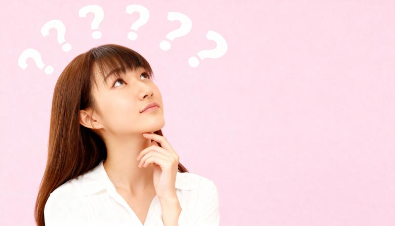 長い茶色の髪と前髪を持ち、白いブラウスを着た若い女性が画像の中央に位置し、無地のピン...。