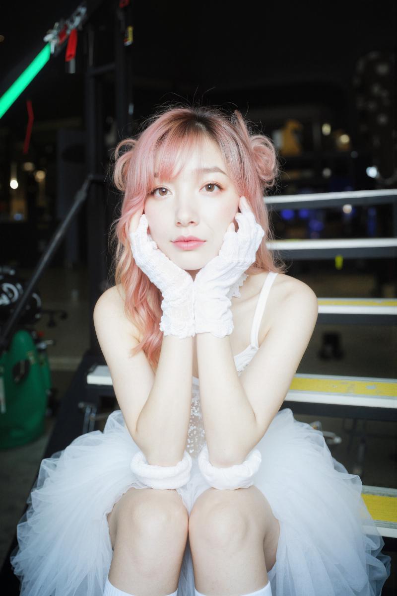 白いチュチュと白い手袋を身に着け、ボクシングのリングのベンチに座っているピンクの髪の...。