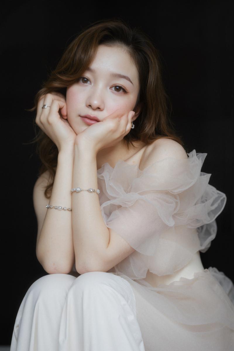 薄手のオフショルダーのトップと繊細なブレスレットを身に着け、あごに手を当てて瞑想的に...。