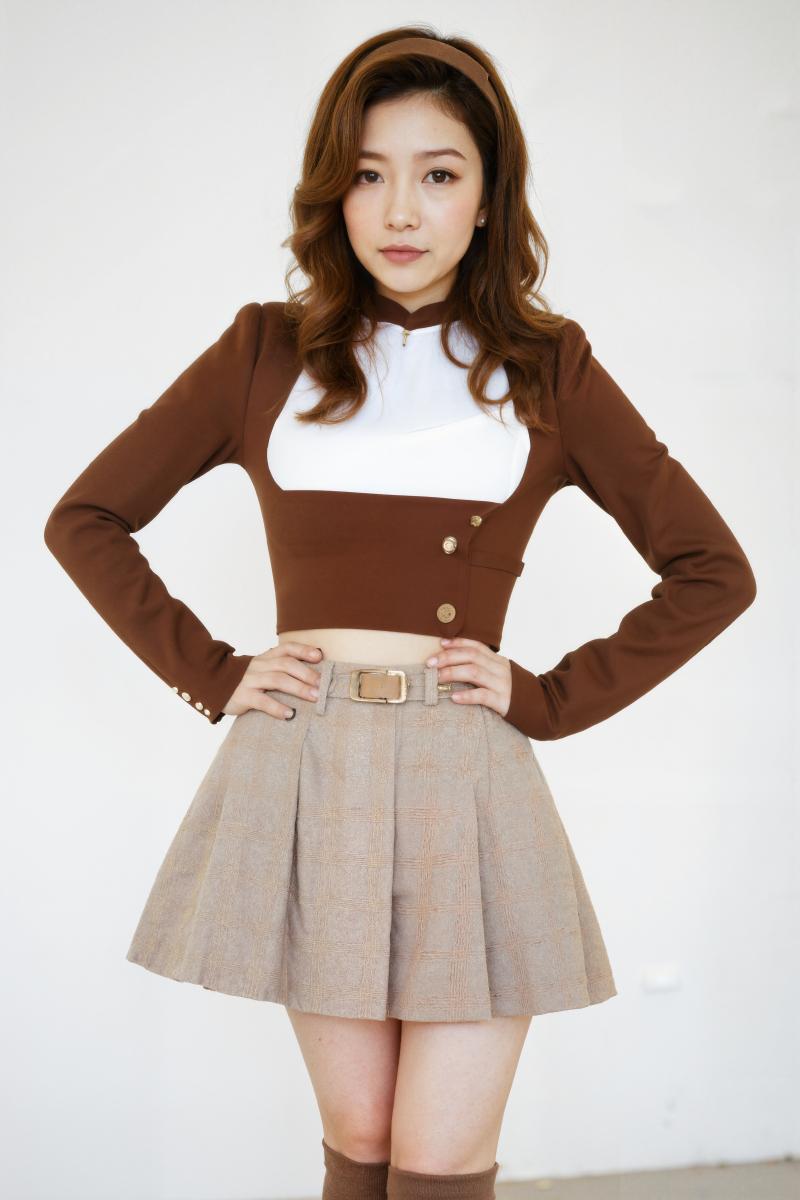 無地の白い壁の前で腰に手を当てて自信満々にポーズをとるアジア系の若い女性。