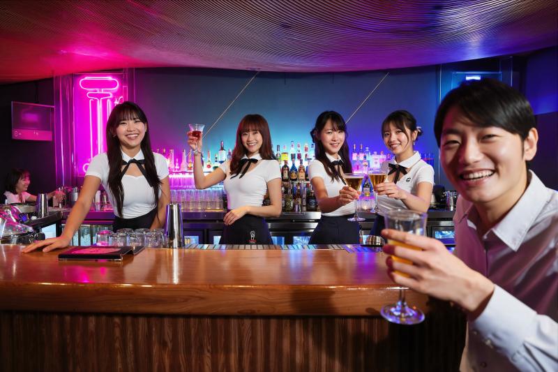 ネオンサインを背景にした薄暗いバーで、バーの後ろに立っている 5 人の若いアジア人女...。