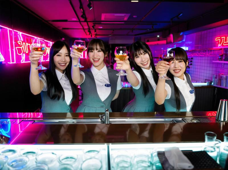 バーカウンターの後ろに立っている 4 人のアジア人女性が、それぞれ異なる色の飲み物の...。