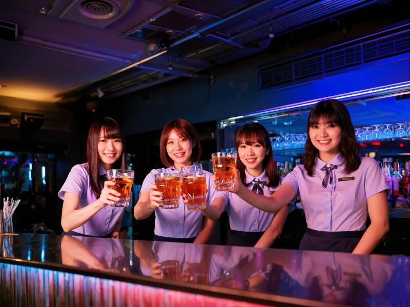 バーの後ろに立ち、ビールのグラスを手にカメラに向かって微笑む 4 人の若い女性を正面...。