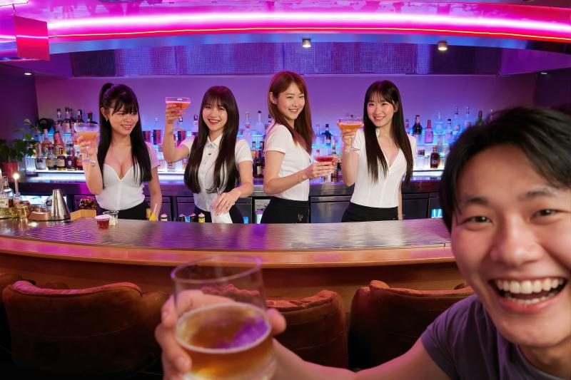 バーの前でビールのグラスを持った若いアジア人男性とその後ろに 4 人の女性バーテンダ...。