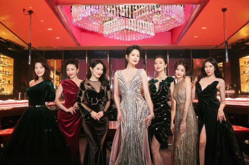 高級宝石店に立ち、大きなピンクのシャンデリアの前で写真を撮る 7 人の女性のグループ。