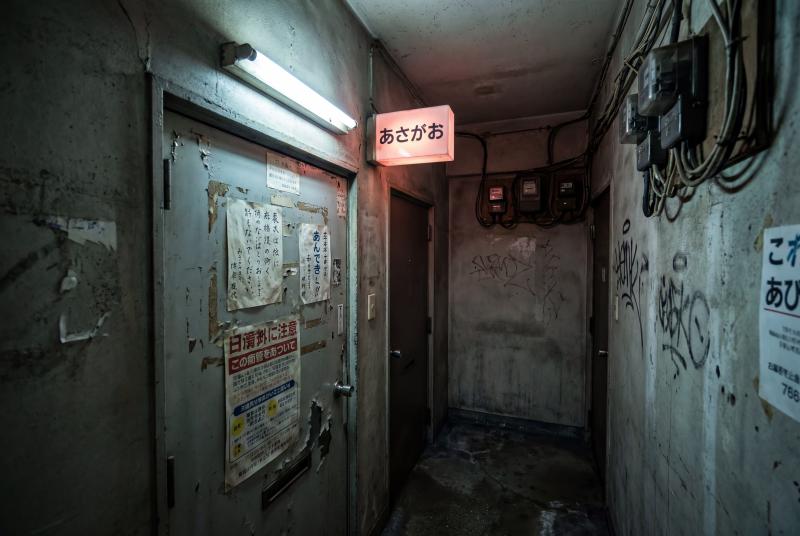 コンクリートの壁が剥がれ落ち、落書きされた廃ビルの薄暗い廊下。