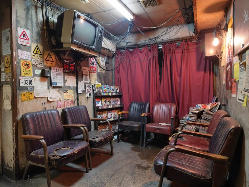 薄暗い部屋で、前景に茶色の革張りの椅子が並び、後ろに赤いカーテンがあり、素朴でビンテ...。