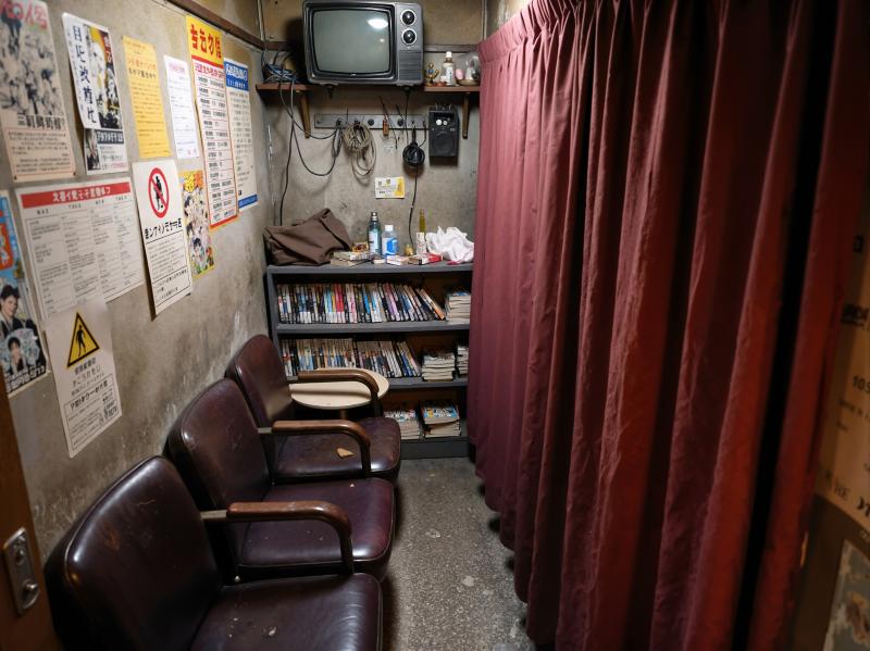 薄暗い部屋の右側に赤いカーテンがあり、壁にはポスターが貼られています。