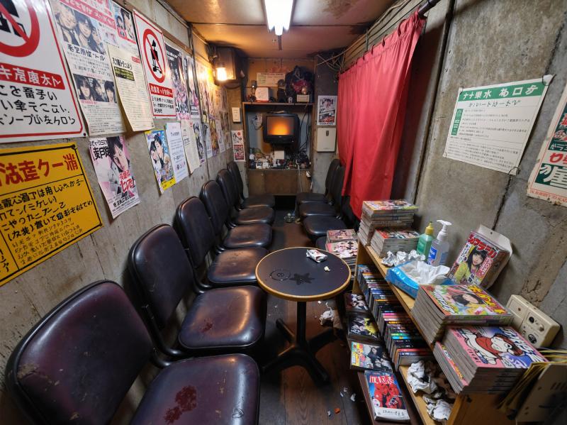 薄暗い部屋の中央に小さなテーブルがあり、その周りには空の椅子が置かれている。