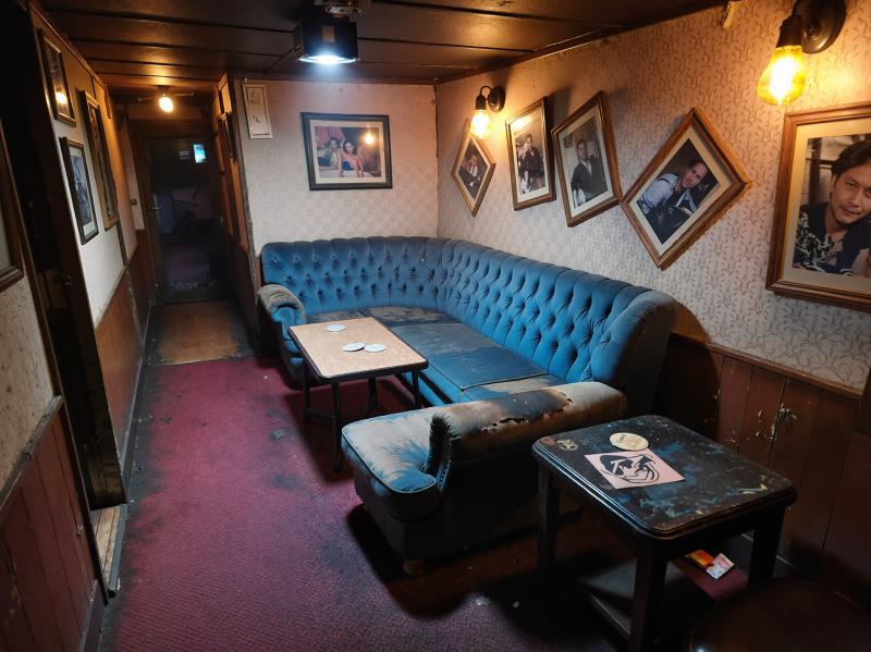 薄暗い部屋の中央に青いベルベットのチェスターフィールドソファがあり、その両側に小さな...。