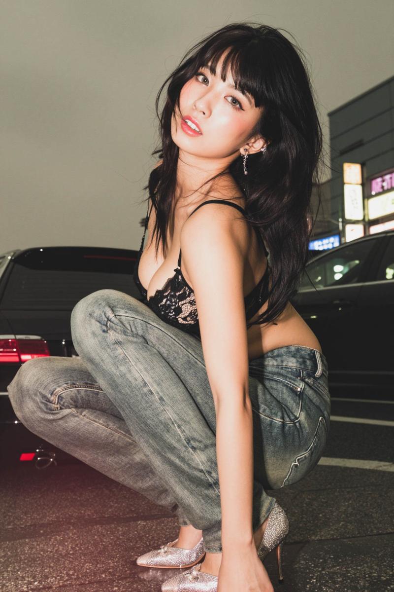 黒いレースのブラジャーとジーンズを着て、夜の街路でしゃがむ若い女性を横から撮影した写...。