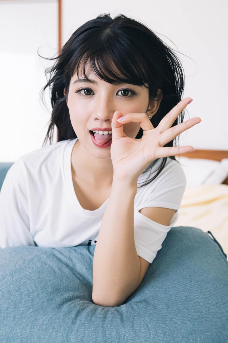 屋内で青いクッションに横たわり、遊び心のある表情でふざけてポーズをとる若い女性を、ク...。