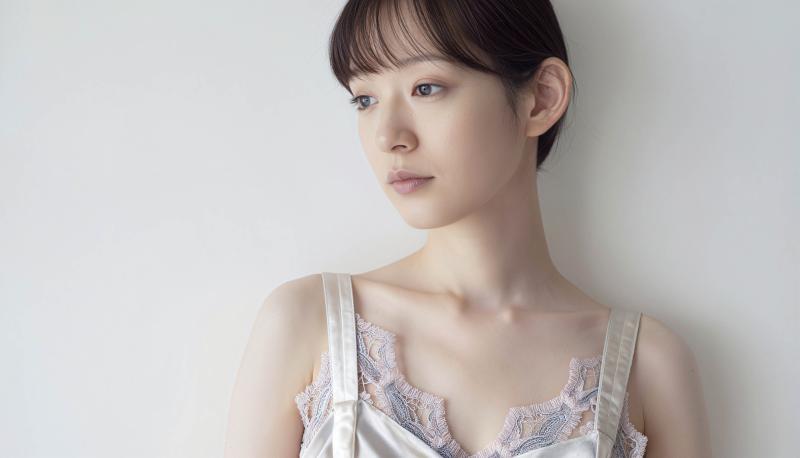 真っ白な壁を背景に撮影された、中性的な表情を持つ若い女性の写実的なポートレート。